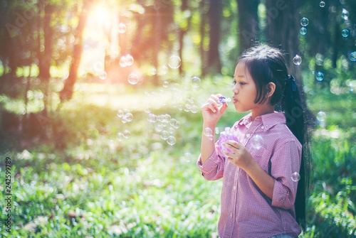Asian girl wearing a pink shirt, being within the Park. She is currently blowing soap bubbles with fun. In the midst of the evening sun, concept of fun and freedom with copy space.