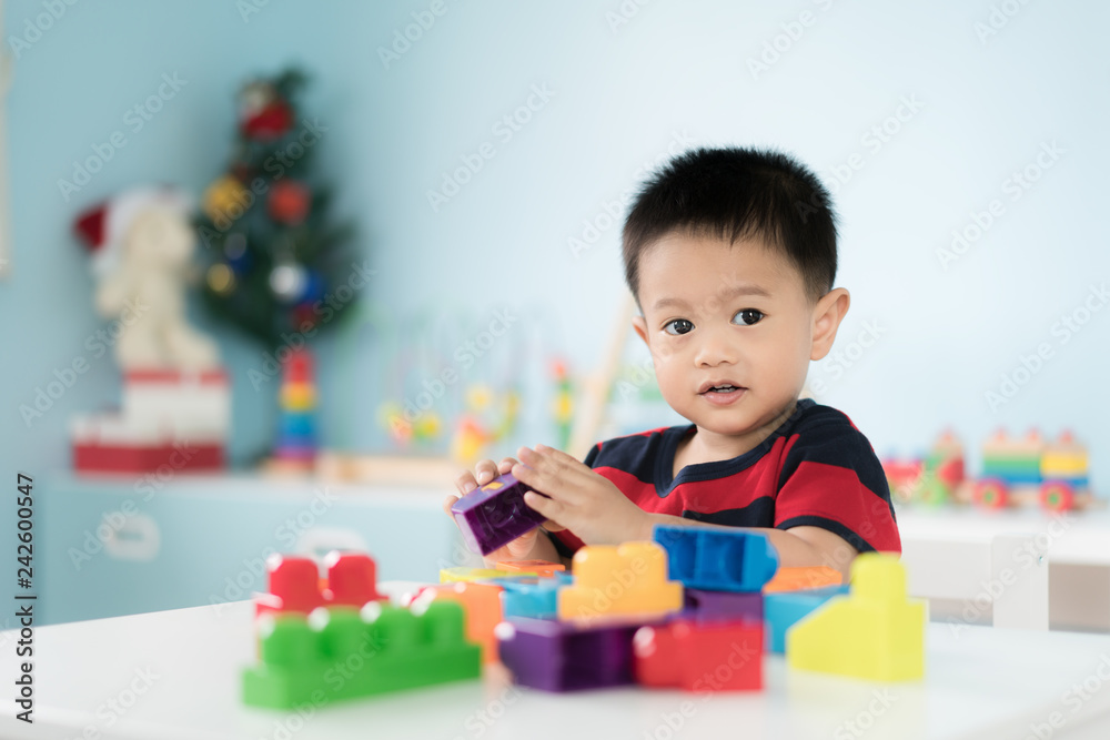 Adorable Asian Toddler baby boy sitting on chair and playing with color block toys at home.. Adorable Asian Toddler baby boy sitting on chair and playing with color block toys at home..