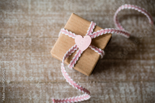 Mit Liebe schenken - Kleines Geschenk mit rosafarbenen Band und Herz auf Holz
