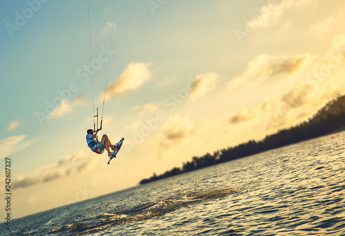 Young man kite boarder jumps over the sea at sunset           