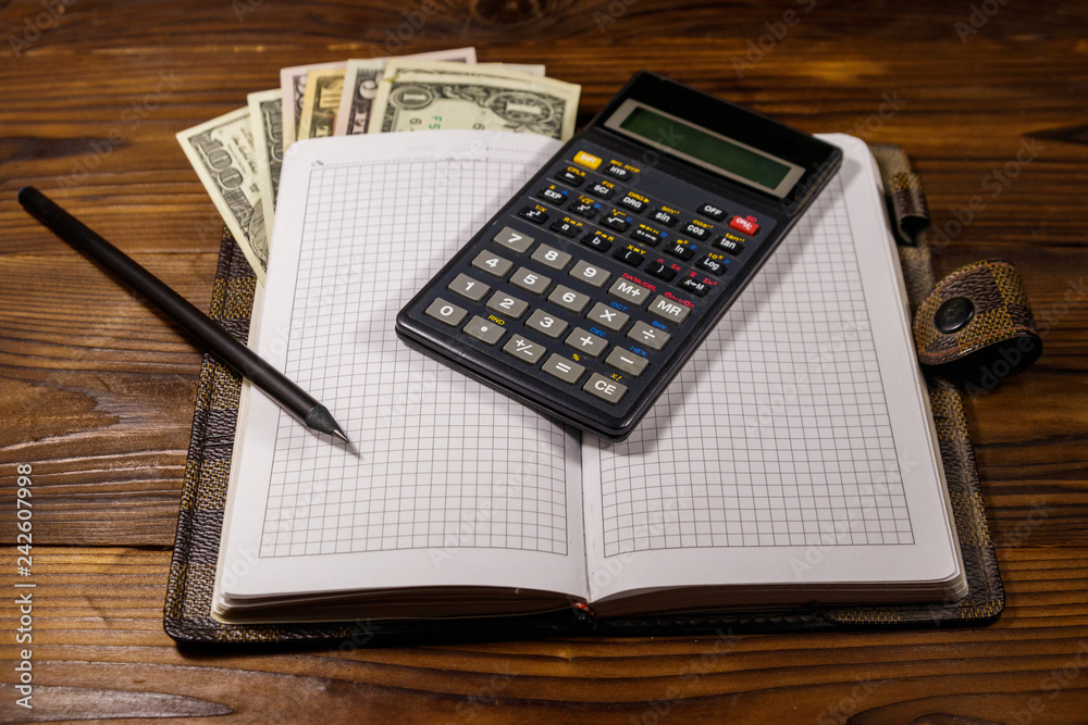 Notepad with dollars, pencil and calculator on wooden desk. Financial planning concept Notepad with dollars, pencil and calculator on wooden desk. Financial planning concept
