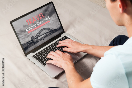 Man searching for travel destinations in a travel agency website with a laptop, sitting at home.