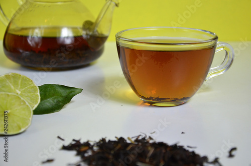 Transparent cup and teapot with black tea, dry tea brewing on the table, bergamot slices, or lemon or lime on a white background