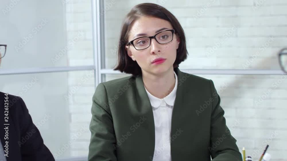 Tracking shot of young businesswomen in glasses and formalwear sitting at table and talking to Arab male job applicant while conducting interview Tracking shot of young businesswomen in glasses and formalwear sitting at table and talking to Arab male job applicant while conducting interview