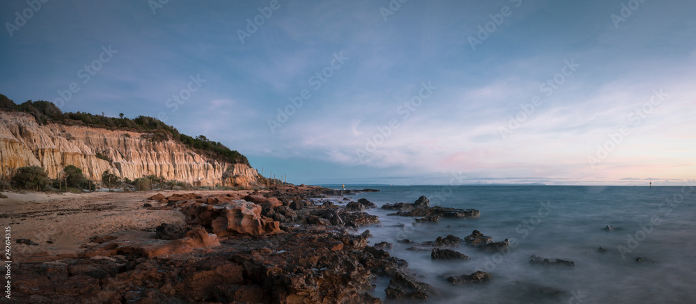 Panoramic Long Exposure Shot of Red Bluff Lookout, a burnt orange-colour cliff,  characterised by the oxidised iron in the cliffs with a rocky beach in the sunset time
