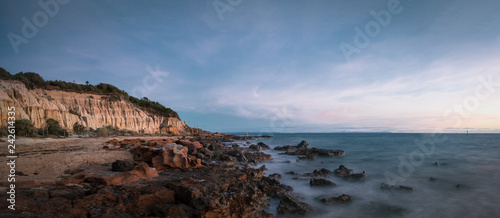 Panoramic Long Exposure Shot of Red Bluff Lookout, a burnt orange-colour cliff, characterised by the oxidised iron in the cliffs with a rocky beach in the sunset time