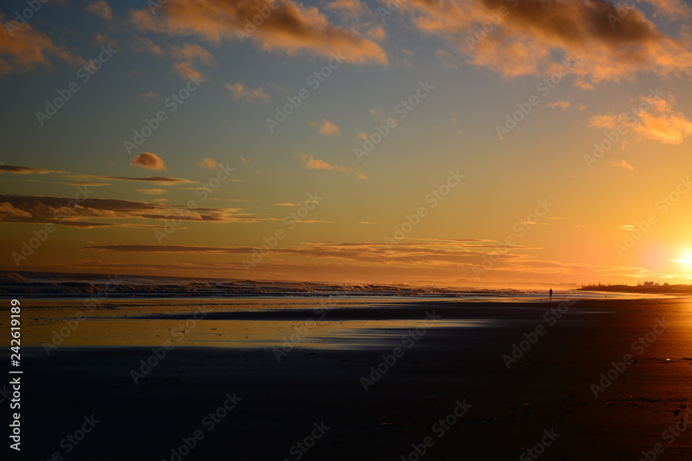 Dramatic sunrise colours; beautiful sunrise on a beach and a lonely figure of a person walking along the beach.
