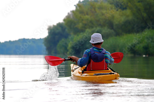 Rear view of kayaker man paddle yellow kayak on Danube river. Summer kayaking. Concept for adventure, travel, action, lifestyle