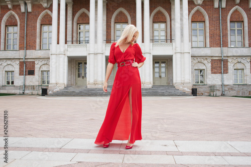 Beautiful and elegant girl in a long red dress stands in the middle of the medieval castle