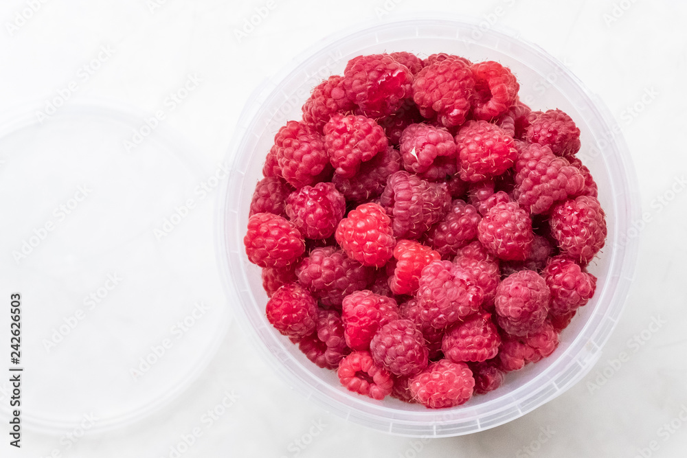 Ripe raspberries in a plastic bucket on a light background Ripe raspberries in a plastic bucket on a light background