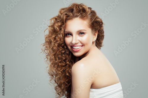 Laughing redhead girl with healthy skin and long healthy curly hairstyle. Smiling girl on gray background