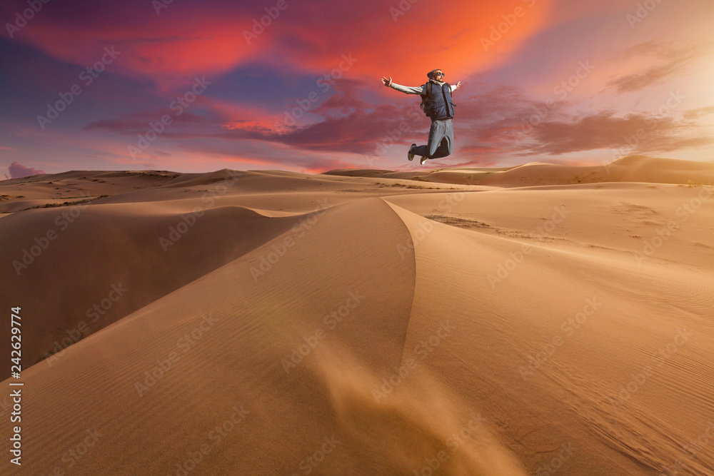 Guy jumping in the desert on a sand dune at sunset.