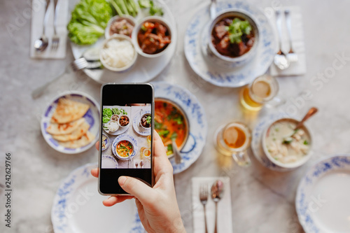 Hand of anonymous female using smartphone to take photos of delicious dishes on table