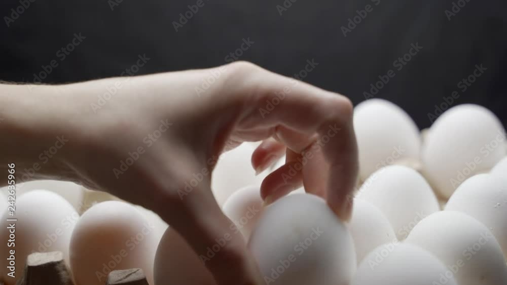 Hand puts eggs in a box. Eggs are stacked in a tray.