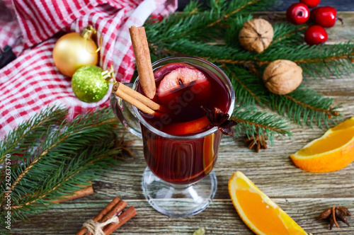 Hot mulled wine in glass mug on a wooden table. Fragrant traditional winter drink based on wine, juice, spices, seasonings, fruits.