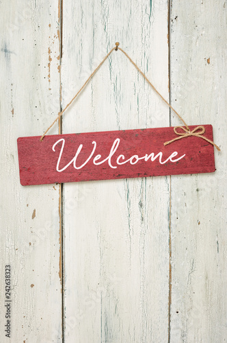 Red sign in front of a white wooden wall - Welcome photo