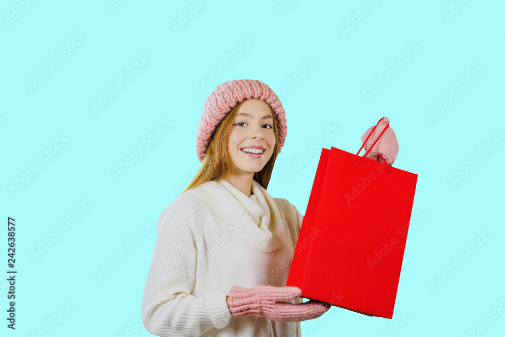 Beautiful young red-haired girl with gift bags after shopping looks into the camera on blue background