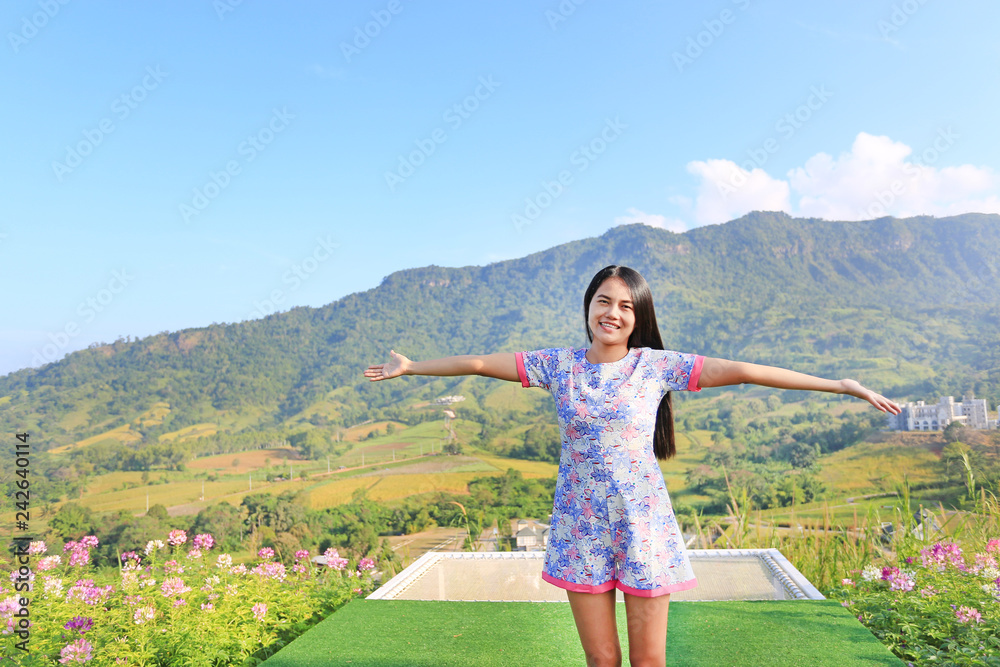 Young Asian woman feeling free with arms wide open at beautiful trees and mountains on blue sky with white puffy cloud.