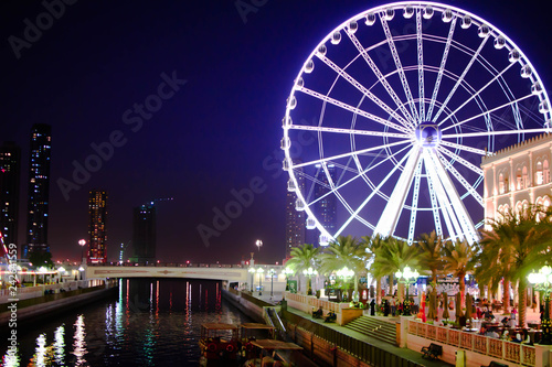 Giant Ferry Wheel and Water Canal in Park with blue sky background at Night