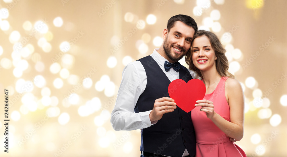 valentines day, love and people concept - happy couple in party clothes with red heart over festive lights background valentines day, love and people concept - happy couple in party clothes with red heart over festive lights background