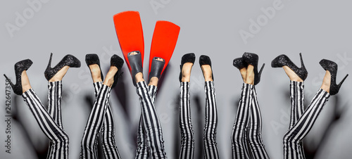 Standing out from others concept. Female sexy legs wearing high heels and one woman wears red flippers isolated over gray background photo
