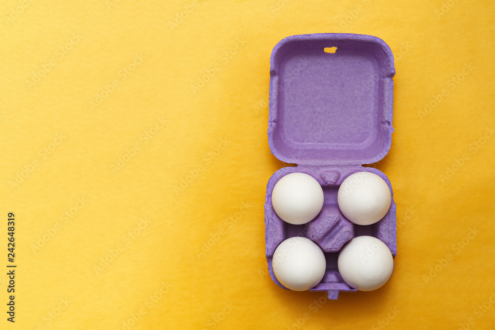 Easter composition. Set of Four white eggs in purple box on yel Easter composition. Set of Four white eggs in purple box on yel
