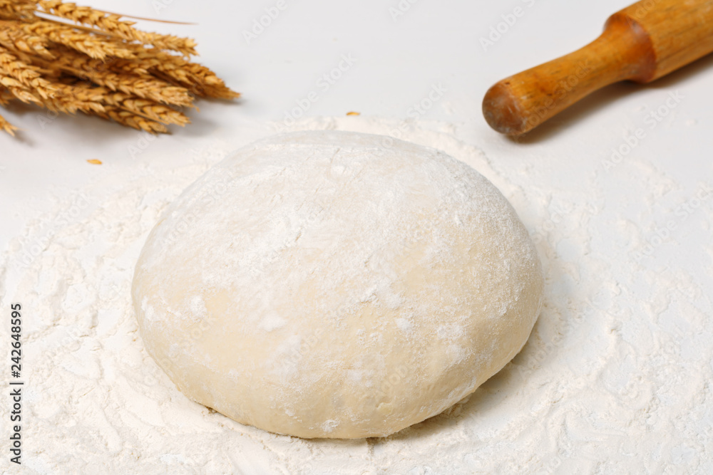 Raw fresh dough in the flour and ears of wheat on a white backgr Raw fresh dough in the flour and ears of wheat on a white backgr
