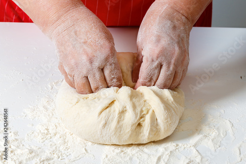 Senior woman kneads raw fresh dough with hands on the table.