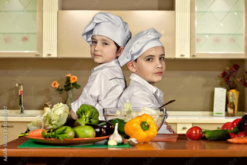 The boys in the cooks costumes cut the salad in the kitchen. Children prepare healthy food. Friendly cooperation of cooks. The boys in the cooks costumes cut the salad in the kitchen. Children prepare healthy food. Friendly cooperation of cooks.