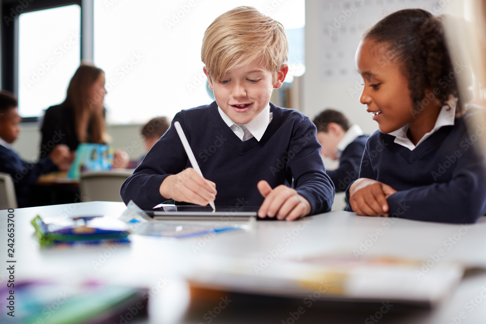 A girl and a boy using a tablet computer and stylus in a primary school class, front view, selective focus A girl and a boy using a tablet computer and stylus in a primary school class, front view, selective focus