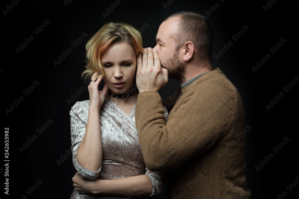 Romantic loving married couple of 30-40 years old share their secrets in the ear against a dark background. Romantic loving married couple of 30-40 years old share their secrets in the ear against a dark background.