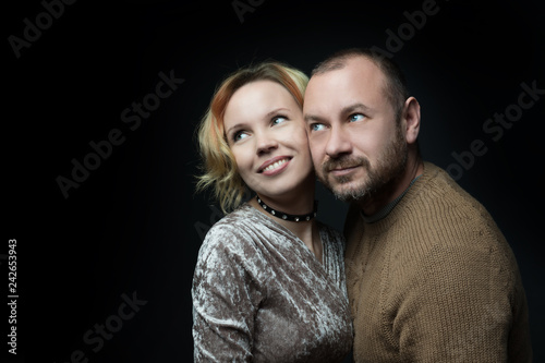 Romantic loving married couple of 30-40 years old are looking one way against a dark background.