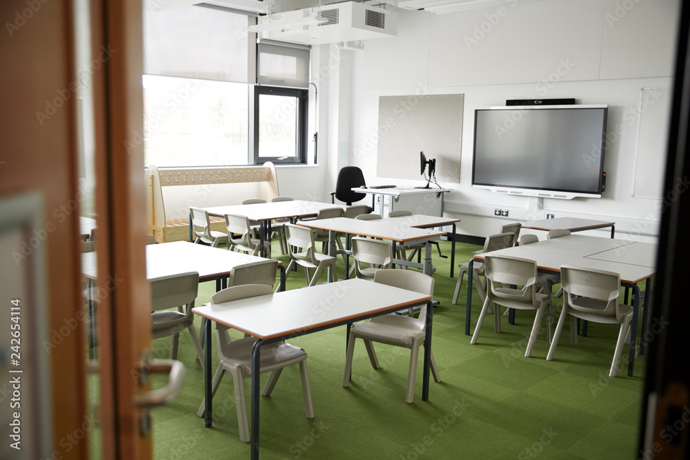 An empty classroom in a primary school with white desks and chairs, seen from doorway An empty classroom in a primary school with white desks and chairs, seen from doorway