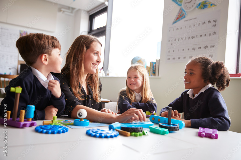 Female teacher and three primary school kids sitting at a table in a  classroom working with educational construction toys, close up, low angle  Stock Photo | Adobe Stock