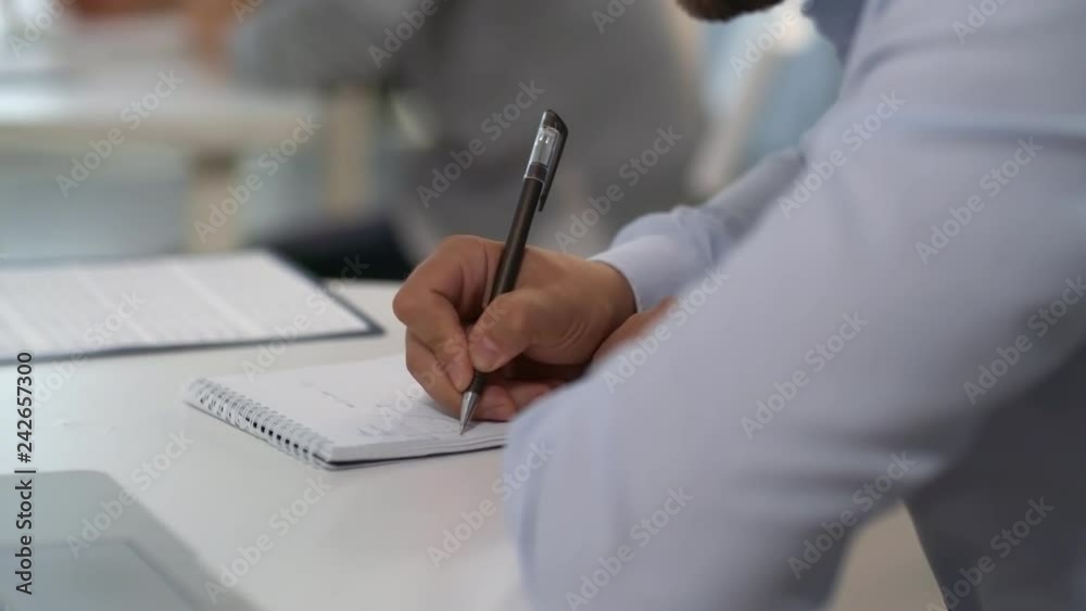 Close-up view of hands of businessman in formal shirt writing down in notepad at desk