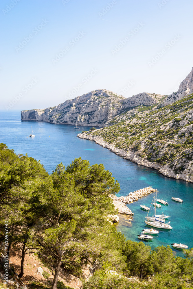 View over the calanque de Morgiou on the mediterranean shore near Marseille, France, with sailboats mooring in the turquoise waters and the cap Morgiou in the distance on a sunny spring day.