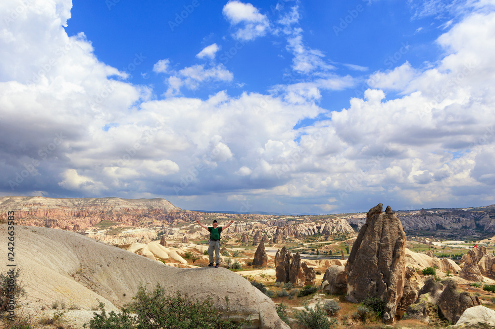 A young man stands on top of a hill and looks up at a cloudy blue sky in Cappadocia.