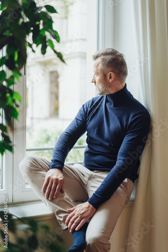 Man looking outside the window, sitting on sill