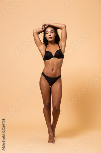 Beauty portrait of sexual woman wearing black lingerie, standing isolated over beige background
