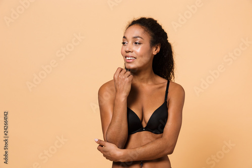 Beauty portrait of sensual woman wearing black lingerie, standing isolated over beige background