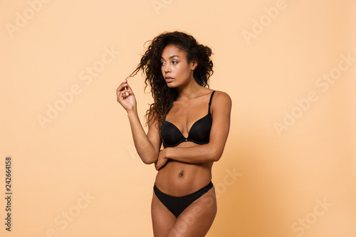 Beauty portrait of sexy woman wearing black lingerie, standing isolated over beige background