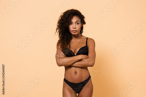 Beauty portrait of charming woman wearing black lingerie, standing isolated over beige background