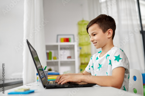 education, technology and people concept - smiling student boy typing on laptop computer at home