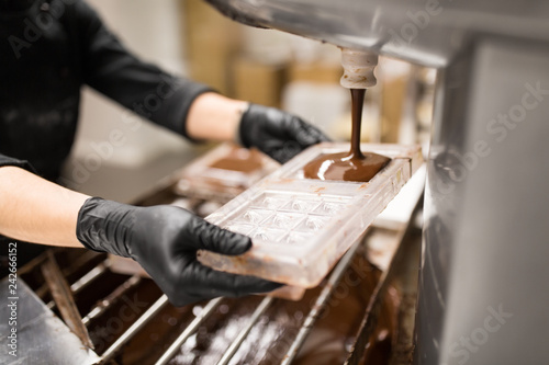 Photography production, cooking and people concept - confectioner filling candy mold with ch