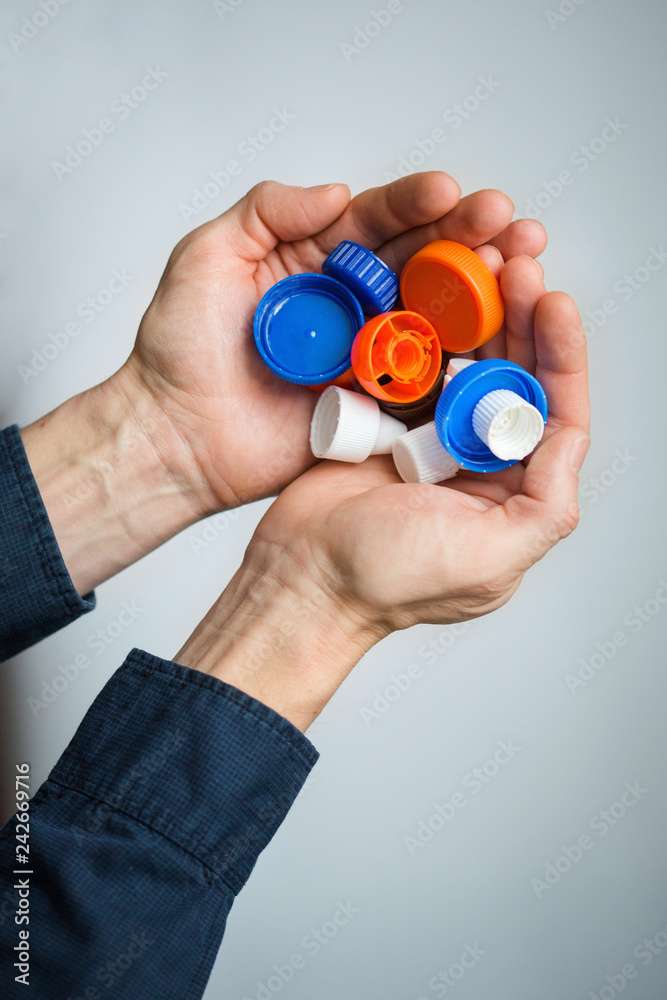 Fototapeta premium two hands with plastic lids on white background. covers are recyclable.