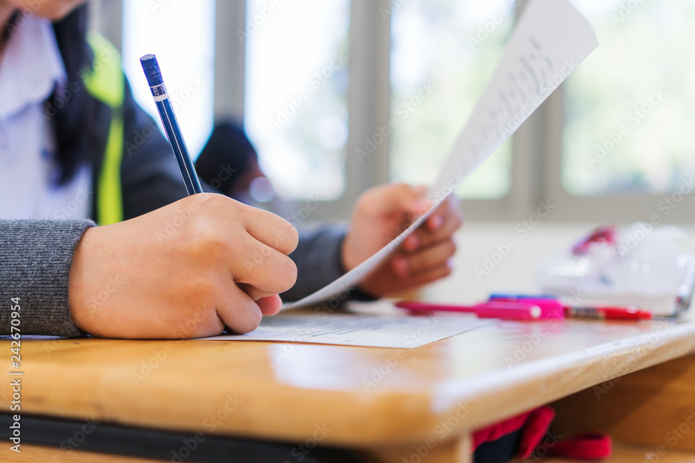 Exams test student in high school, university student holding pencil for testing exam writing answer sheet and exercise for taking in assessment paper on wood table classroom. Education study Concept Exams test student in high school, university student holding pencil for testing exam writing answer sheet and exercise for taking in assessment paper on wood table classroom. Education study Concept