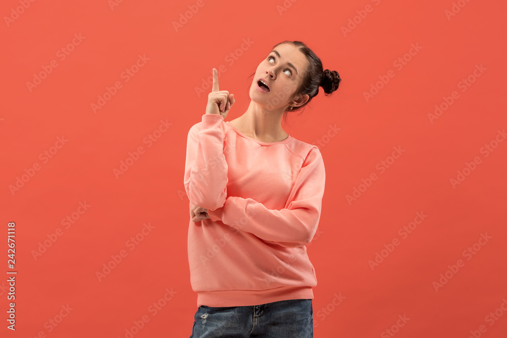 Happy woman standing and smiling isolated on coral studio background. Beautiful female half-length portrait. Young emotional woman pointing up. The human emotions, facial expression concept. Happy woman standing and smiling isolated on coral studio background. Beautiful female half-length portrait. Young emotional woman pointing up. The human emotions, facial expression concept.