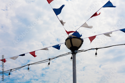 Festivity Flag and Stringed Bulbs Hanging Horizontally from Lamp Post. Different Color Banner for Attraction. Decoration Ideas in Celebrating an Occasion