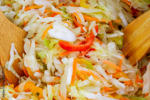Preparation of vegetarian salad of fresh raw vegetables (white cabbage, carrots, red sweet pepper) Mixing with two wooden blades. The concept of healthy eating. Macro photography