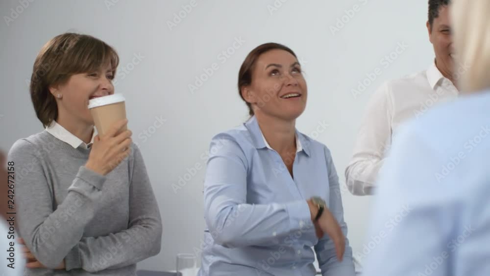 Joyous middle aged female manager telling funny story to colleagues on coffee break; employees standing in circle and laughing Joyous middle aged female manager telling funny story to colleagues on coffee break; employees standing in circle and laughing